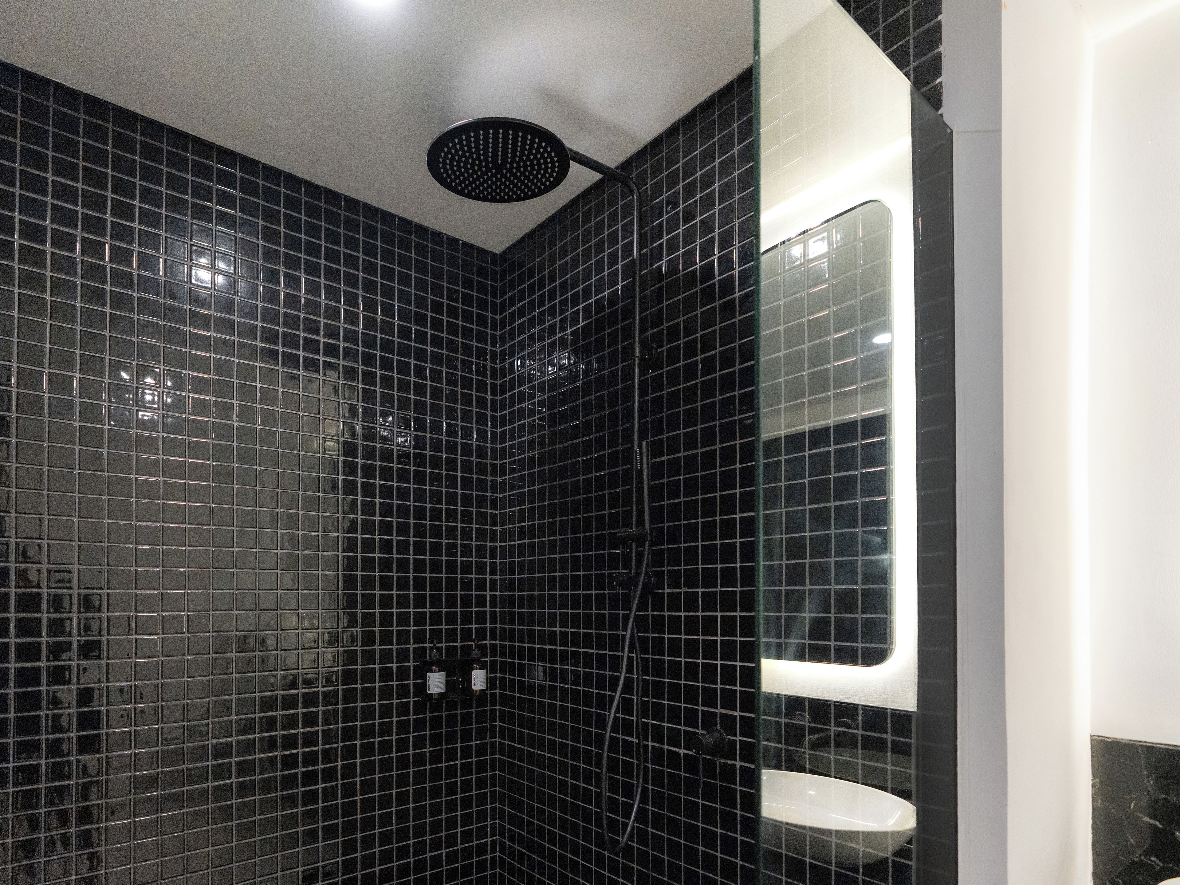 A bathroom with black tiled walls, a showerhead, and a white sink.