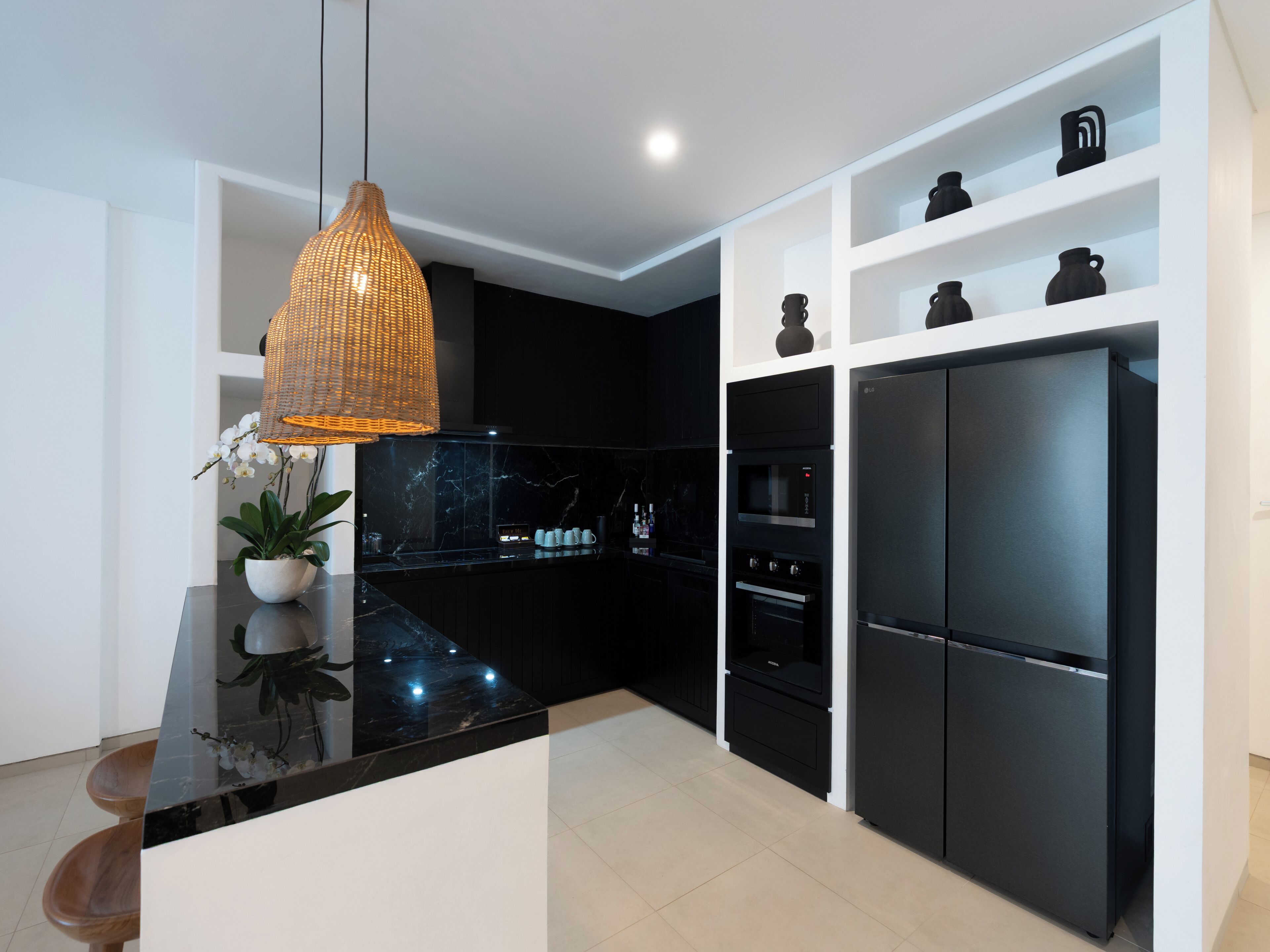 A modern kitchen with black cabinets, a black refrigerator, and a hanging pendant light.