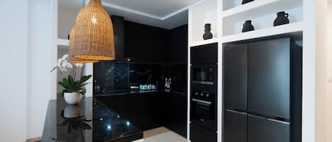 A modern kitchen with black cabinets, a black refrigerator, and a hanging pendant light.