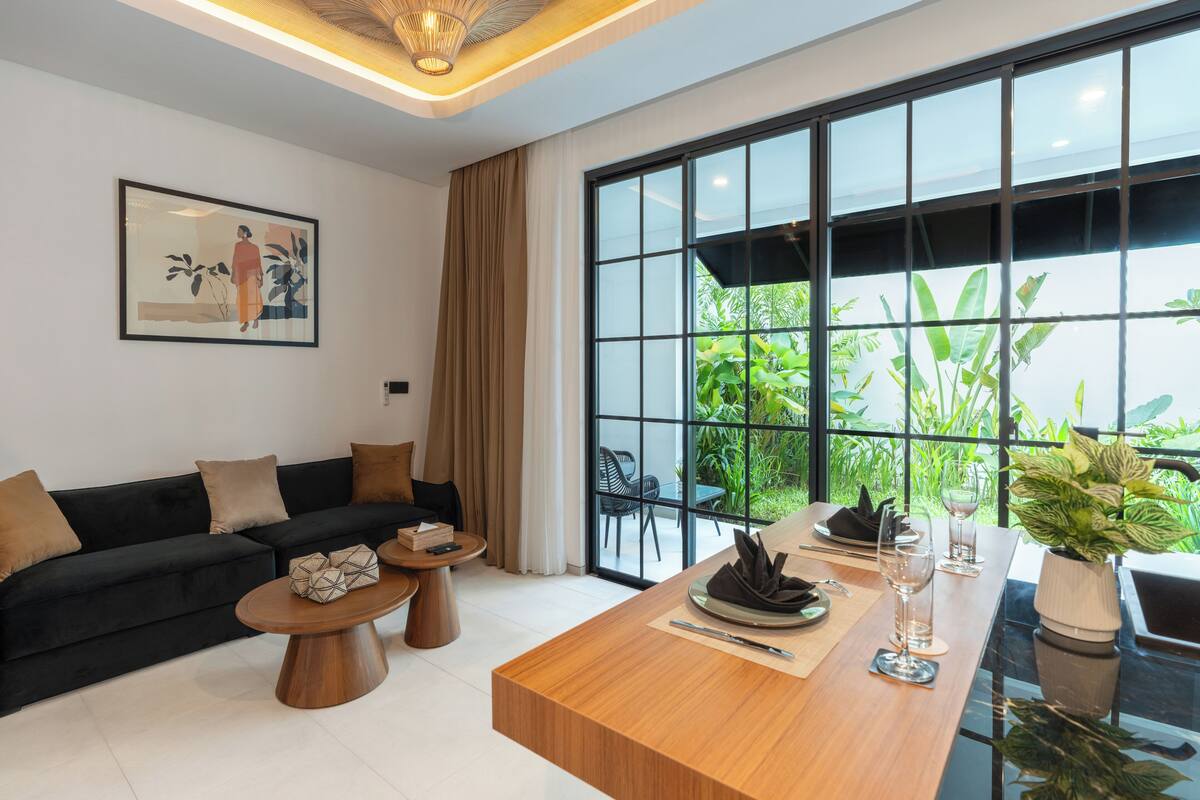 Ein modernes Wohnzimmer mit einer Couch, Couchtisch, Esstisch und großen Fenstern mit Blick auf Grünflächen.