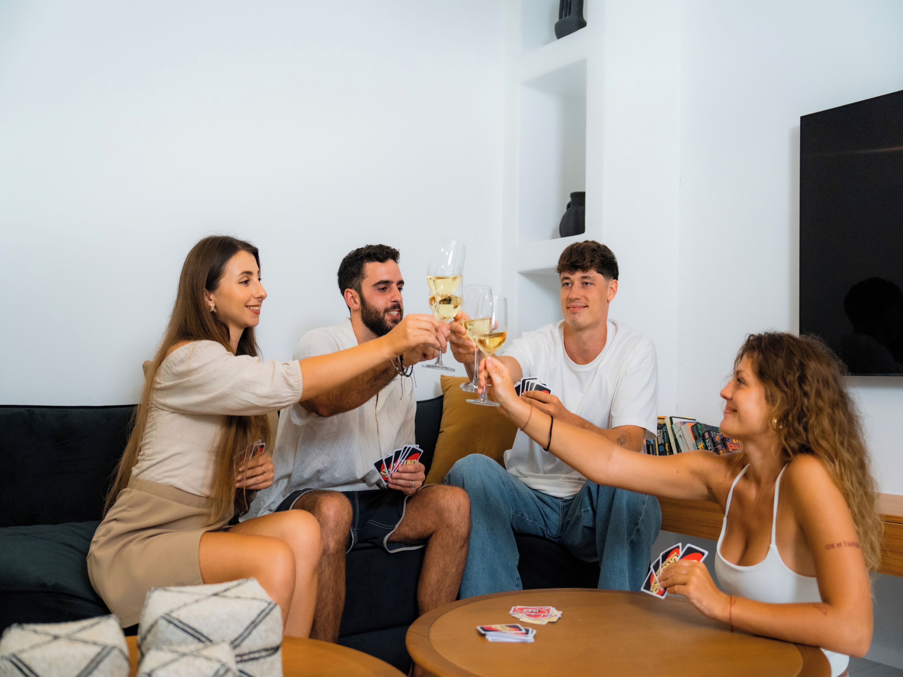 A group of people toasting with champagne glasses, seated around a small round table with playing cards.