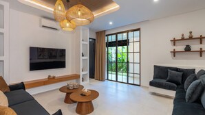 A modern living room with a flat-screen TV, two wooden coffee tables, a sofa, and a large sliding glass door leading to a garden.