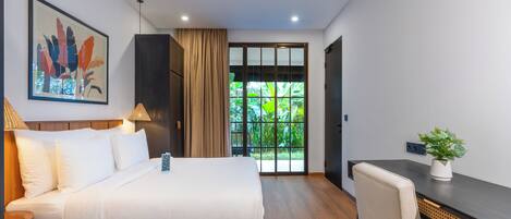 Quarto de hotel moderno com cama, escrivaninha, cadeira e vista para o verde pela janela.