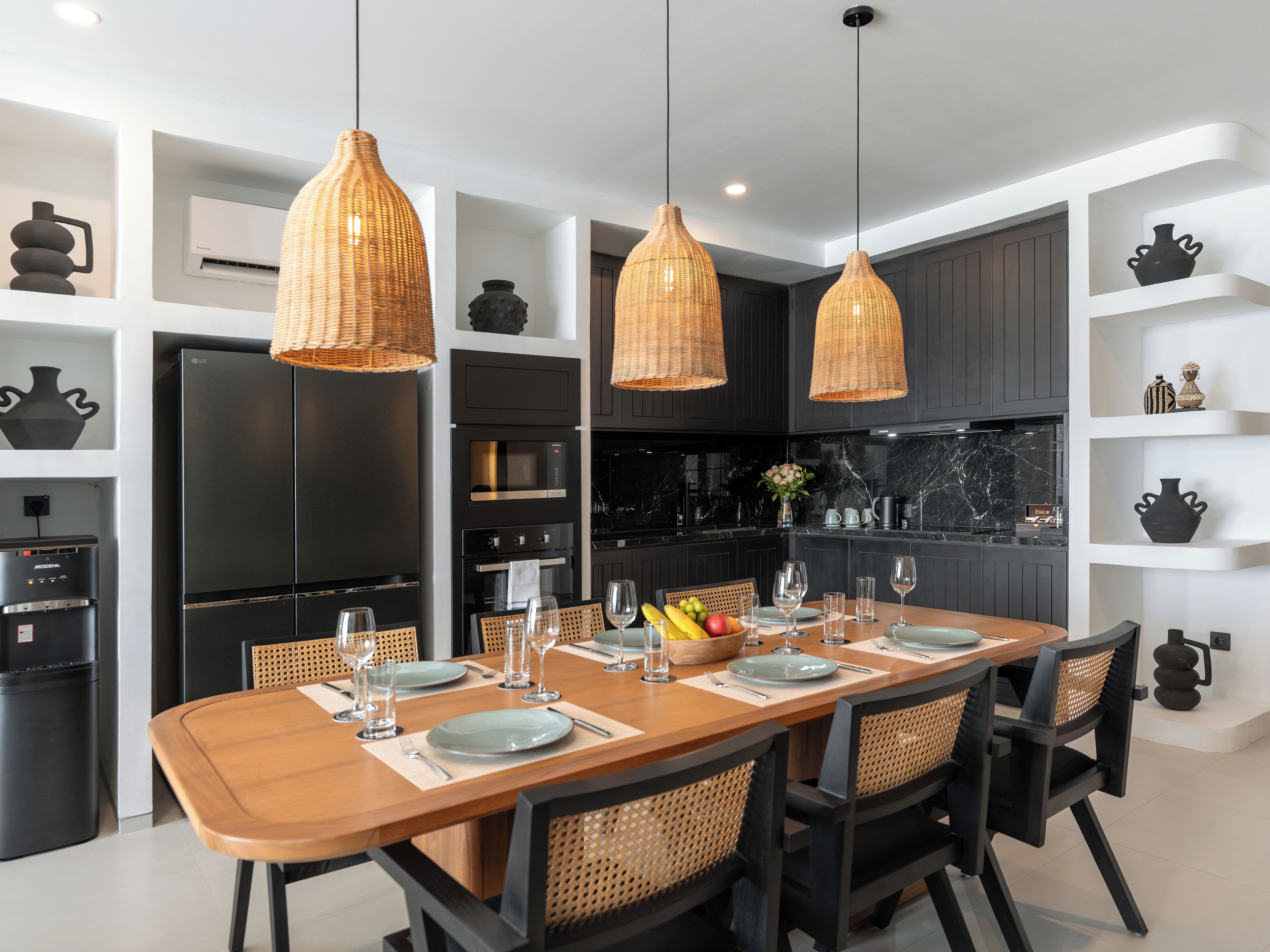 Una cocina moderna con una mesa de comedor preparada para seis personas, que incluye un refrigerador negro, horno empotrado y encimera de mármol.