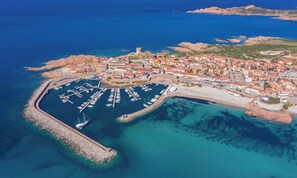Vue aérienne d’une ville côtière avec un port de plaisance, des bâtiments et une tour imposante.