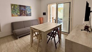 Quarto com mesa de madeira, duas cadeiras, sofá cinza e um quadro na parede.