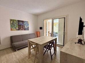 Une pièce avec une table en bois, deux chaises, un canapé gris et un tableau accroché au mur.