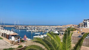 Uma marina com barcos atracados, um muro de pedra e um céu azul límpido.