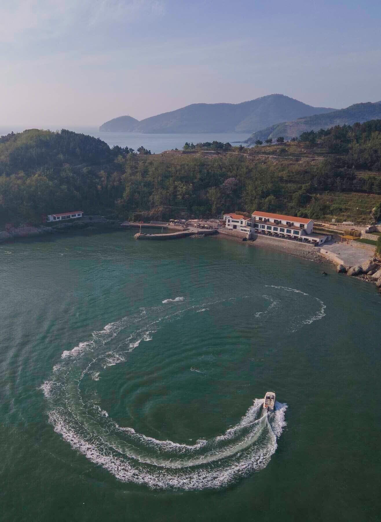 A coastal area with a marina, a building with a red roof, and a boat creating a wake in the water.