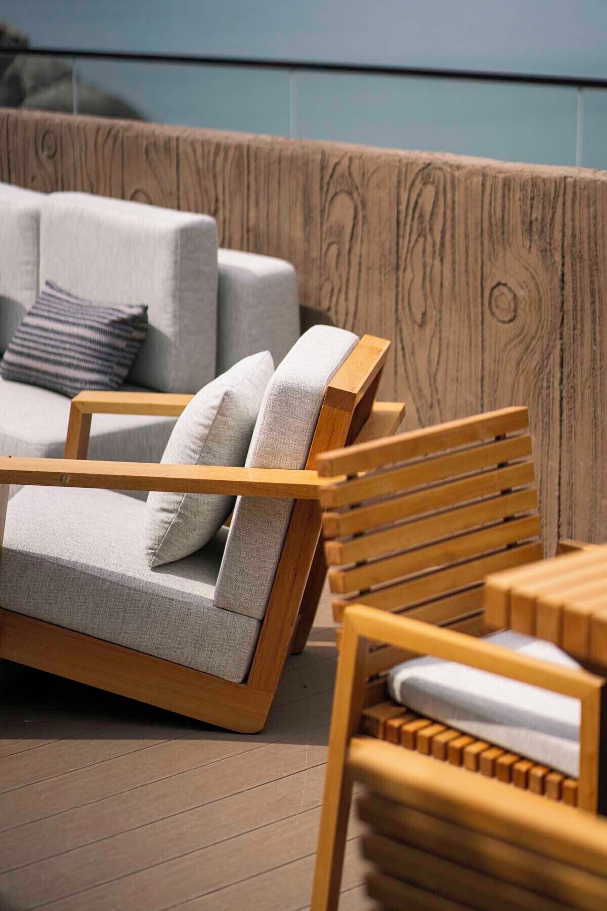 A wooden deck with a sofa and chairs, a wooden wall, and a view of the sky.