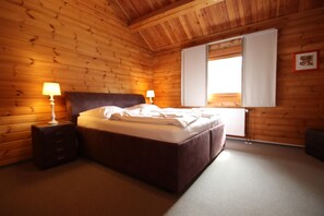 A wooden-paneled bedroom with a bed, two bedside lamps, and a window with curtains.