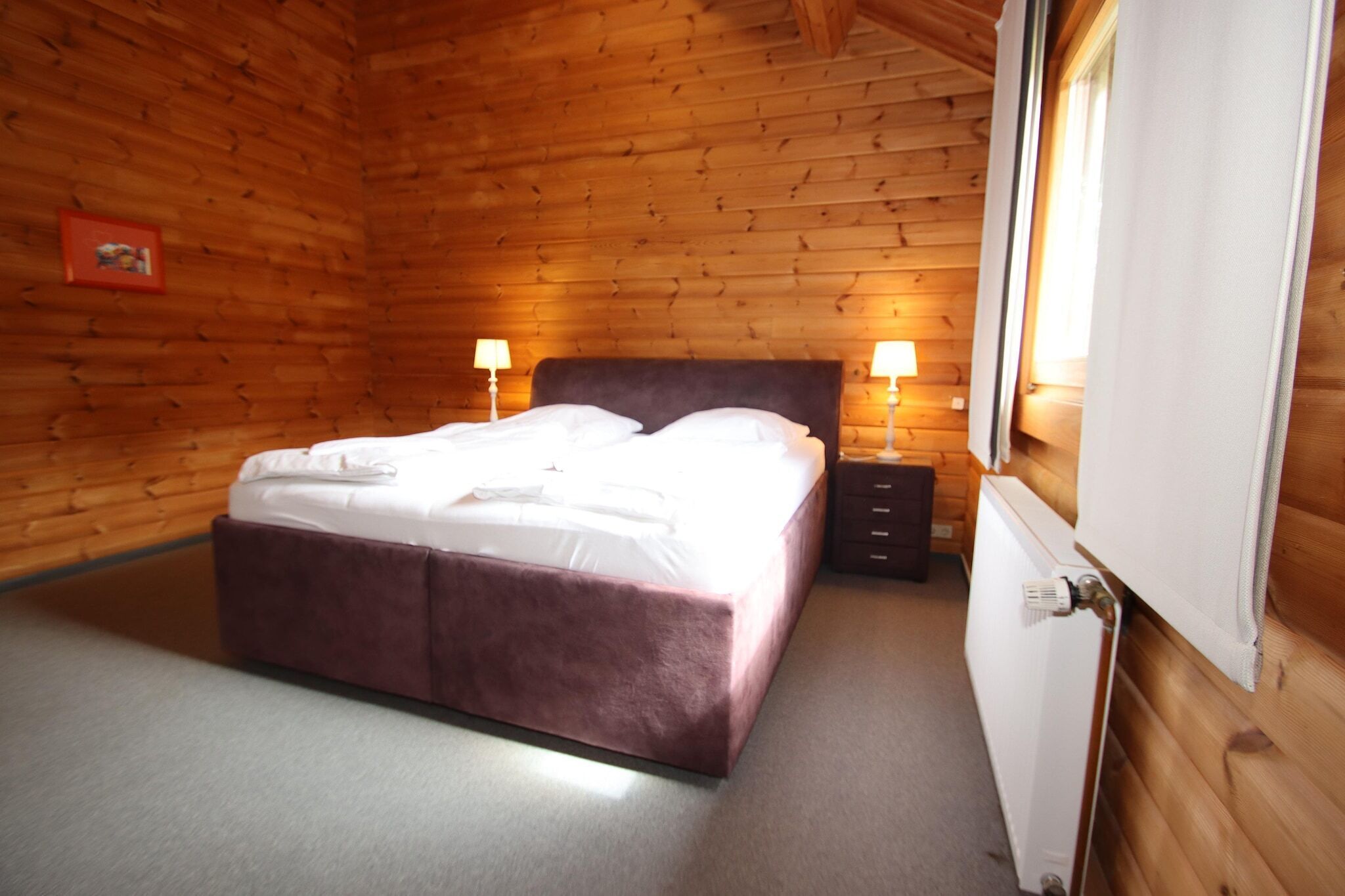 Ein Zimmer mit Holzwandverkleidung, einem Bett, zwei Nachttischlampen und einer Heizung.