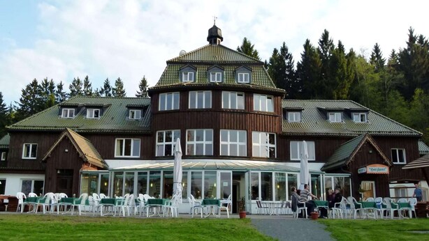 A large building with a central glass-roofed patio area, surrounded by white chairs and tables.