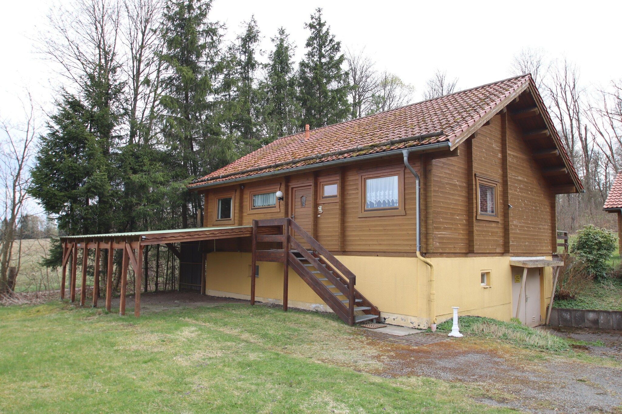 A wooden house with a tiled roof, a wooden staircase, and a covered porch.
