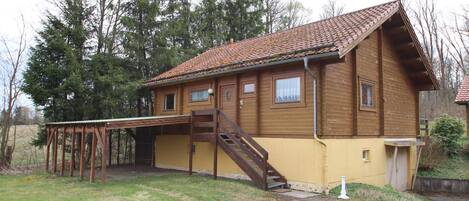 A wooden house with a tiled roof, a wooden staircase, and a covered porch.