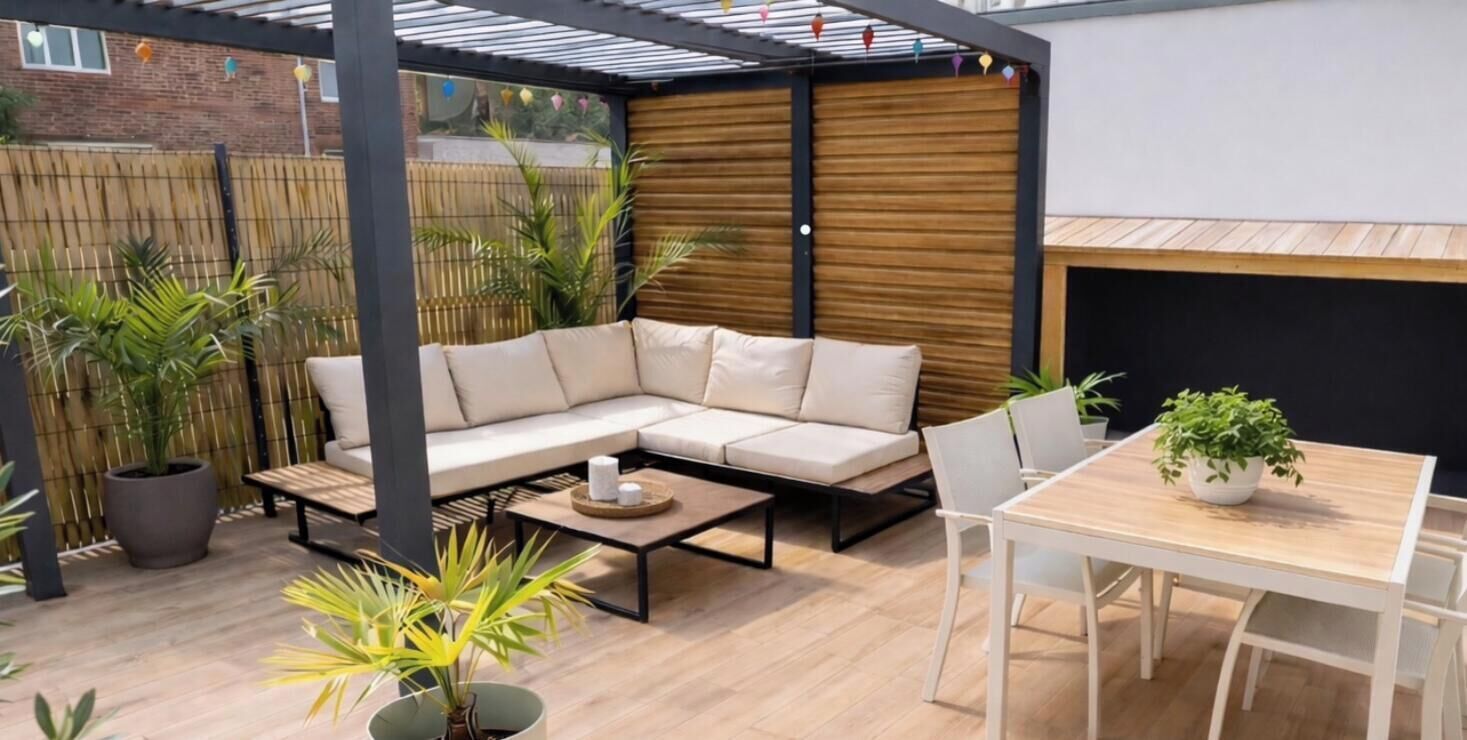 Un patio abrité avec un canapé d’angle, une table en bois et des plantes en pot.