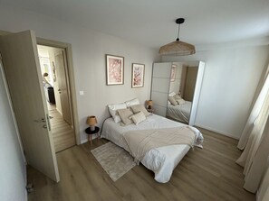 Une chambre à coucher avec un lit, des lampes de chevet, un tapis, un miroir et une porte donnant sur une autre pièce.