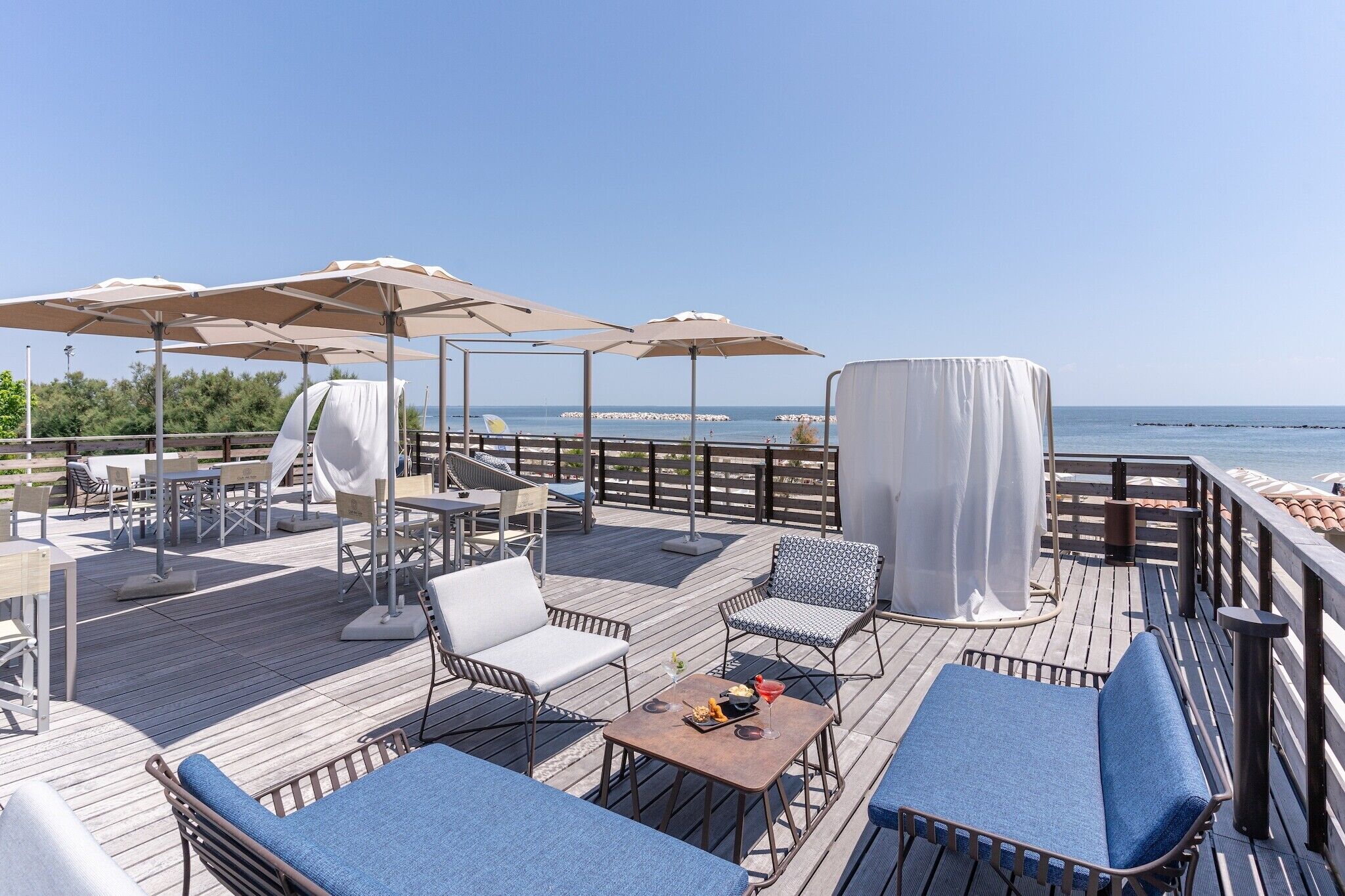 Terraza con asientos exteriores, sombrillas y vista al mar.