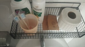 Metallinen hylly, jossa on hygieniatarvikkeita, kuten shampoopullo, saippuapala, hammasharja, kuppi ja wc-paperirulla.