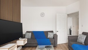 Ein modernes Wohnzimmer mit Flachbildfernseher, zwei Sofas, einem Couchtisch und einer Wanduhr.