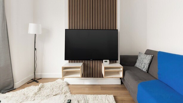 Ein modernes Wohnzimmer mit einem Flachbildfernseher, einem blauen Sofa und einem weißen Teppich.