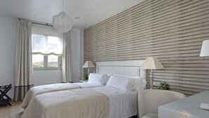 Una habitación de hotel moderna con dos camas, un escritorio, una silla y un ventanal con cortinas.