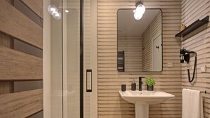 Un baño moderno con cabina de ducha de vidrio, lavamanos pedestal y espejo con fondo de panel de madera.