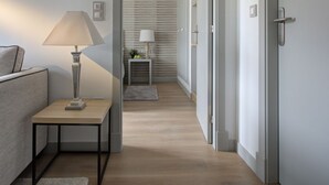 Habitación de hotel moderna con sofá, una mesita con lámpara, una mesita de noche con lámpara y una puerta que conduce a otra habitación.