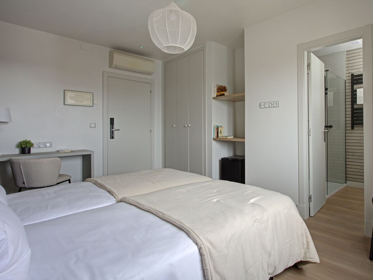 A bedroom with two beds, a desk, a chair, a wardrobe, and a shower area.