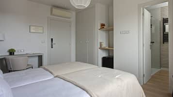 A bedroom with two beds, a desk, a chair, a wardrobe, and a shower area.