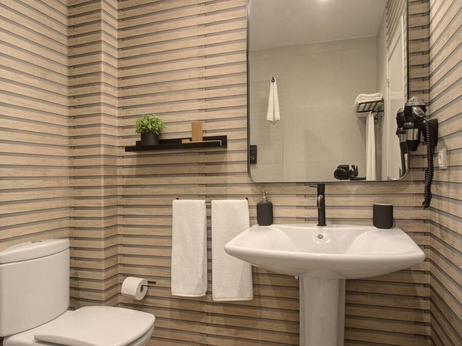 A bathroom with a striped wall design, a white sink, a toilet, two towels, a mirror, and a shelf with a plant and a soap dispenser.