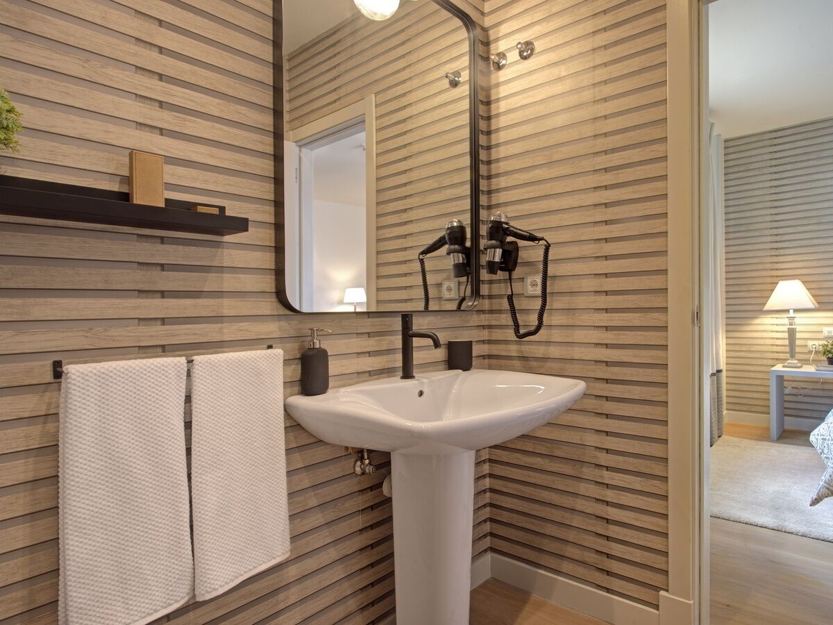 A bathroom with a white sink, a mirror, and wooden paneling on the walls.