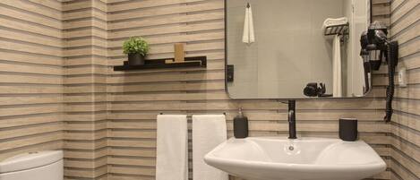 A bathroom with a striped wall design, a white sink, a toilet, two towels, a mirror, and a shelf with a plant and a soap dispenser.