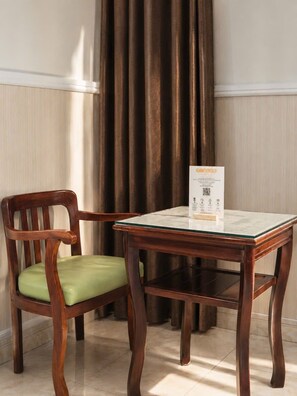 A wooden chair with a green cushion and a glass-top table with a printed card on it. - Sevendays Hotel (My Hanh)