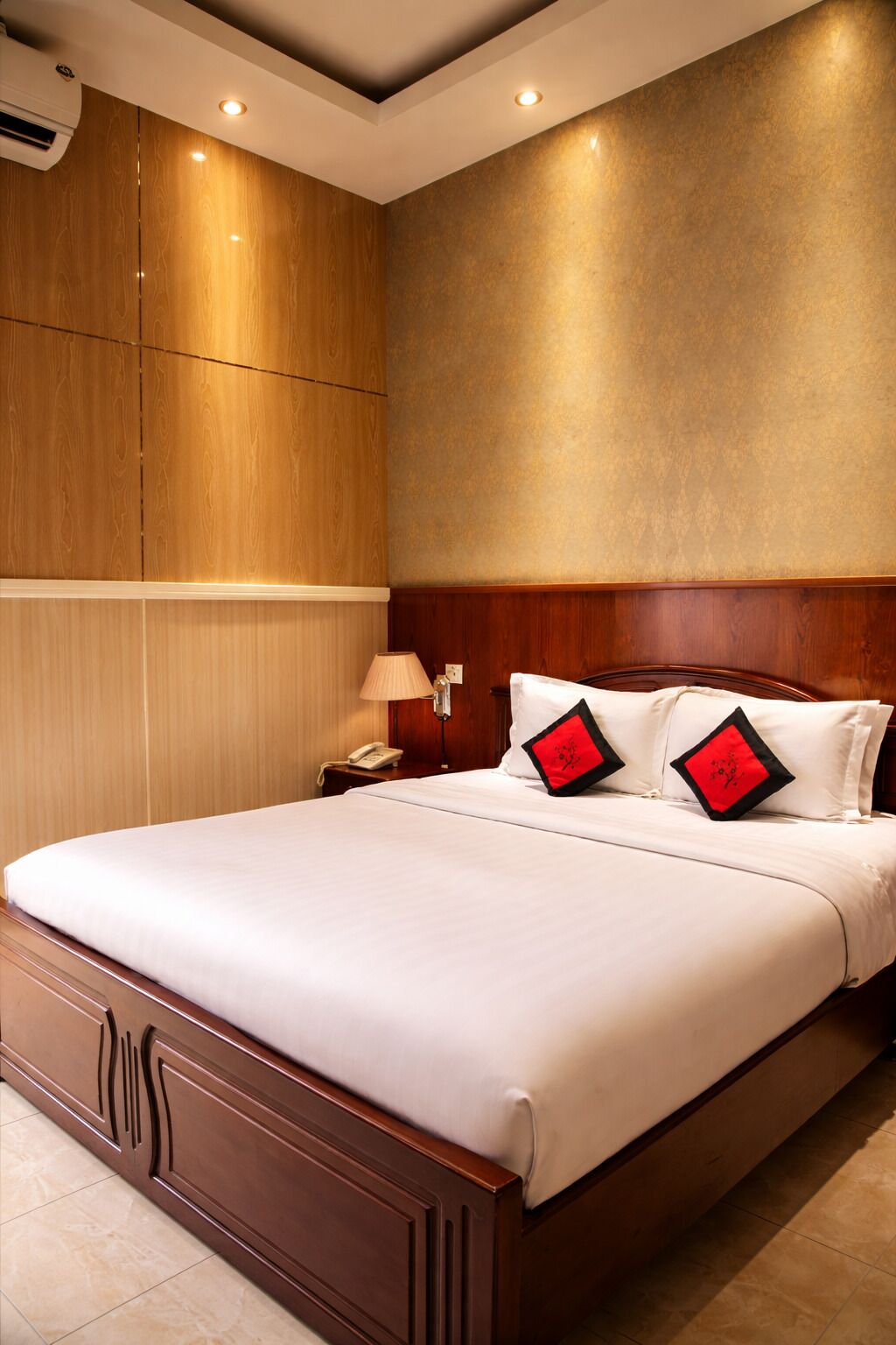 A hotel room with a large bed, wooden headboard, and a wall-mounted air conditioning unit.