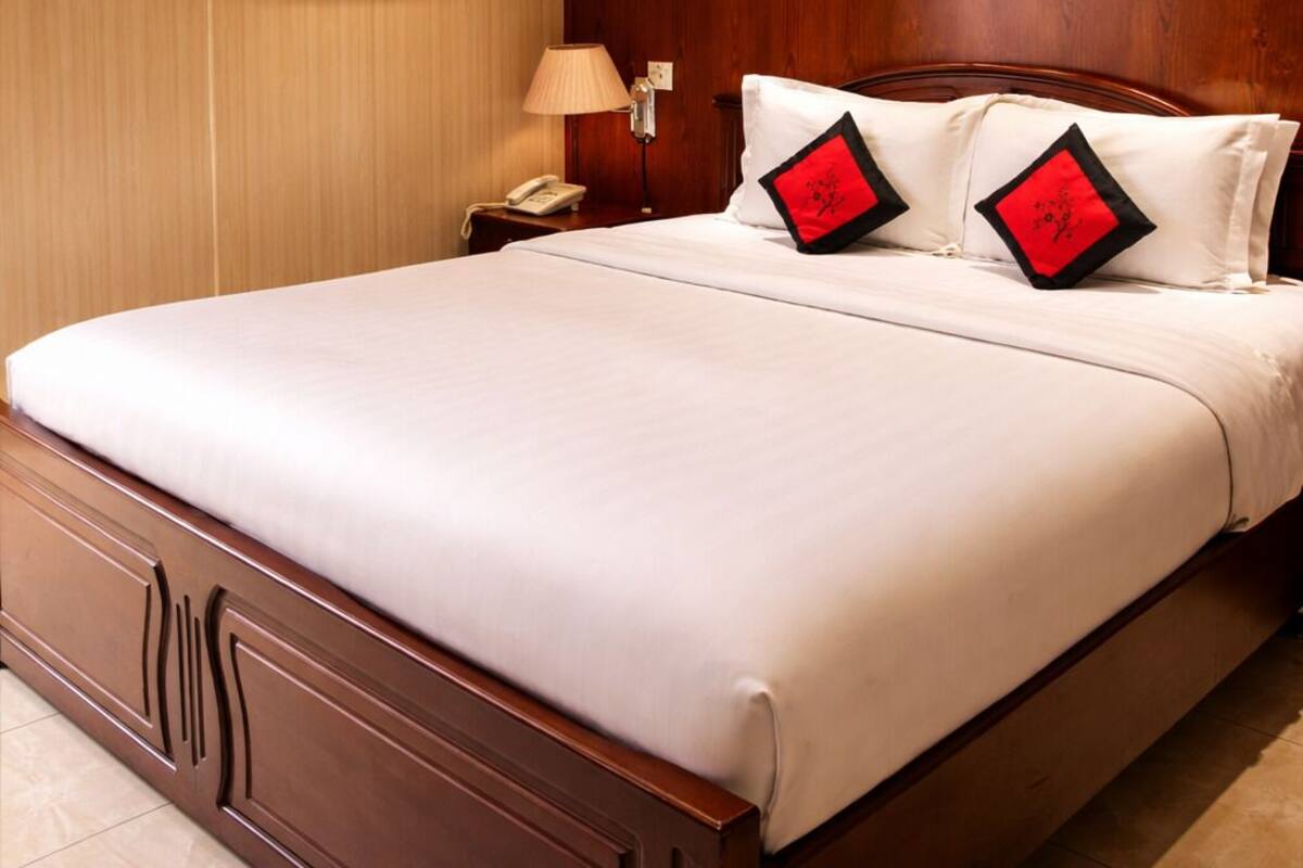 A hotel room with a large bed, wooden headboard, and a wall-mounted air conditioning unit.