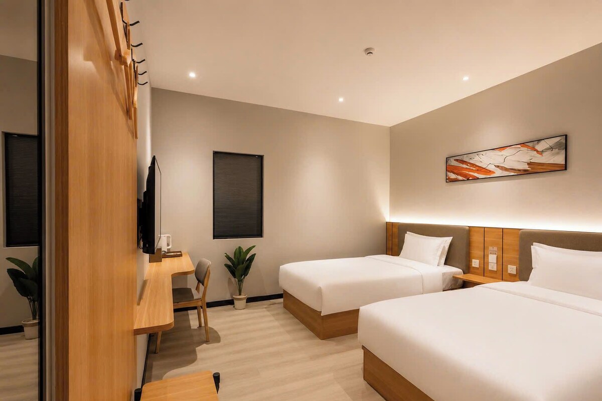 A hotel room with two beds, a desk, a chair, a TV, and a painting on the wall.