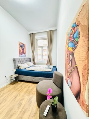 A bedroom with a bed, a sofa, a small table with a plant, a remote control, and a painting on the wall. - Stylish 9BR Apartment for 18 Guests (Vienna)