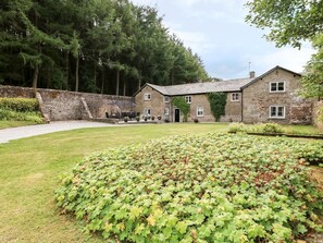 A stone building with a paved driveway, a grassy lawn, and a garden with green foliage. - The Bothy, Wildboarclough (Macclesfield)
