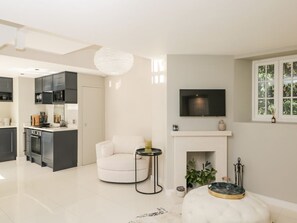 A modern living room with a fireplace, a flat-screen TV mounted above it, a white sofa, and a kitchen area in the background.