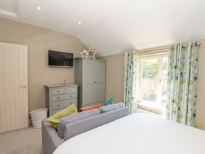 Une chambre à coucher avec un lit, une armoire grise, une télévision et une fenêtre avec des rideaux.