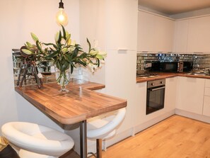 Eine moderne Küche mit Holzarbeitsplatte, weißen Barhocker, Backofen und Mikrowelle.