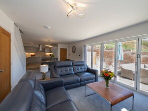 Ein modernes Wohnzimmer mit einer Couch, einem Couchtisch und Blick auf die Küche sowie eine Terrasse.