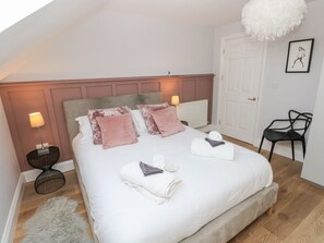 A bedroom with a bed, bedside lamps, a chair, a door, and a radiator. - Cambrie: A Cozy Retreat in Tenby (Tenby)