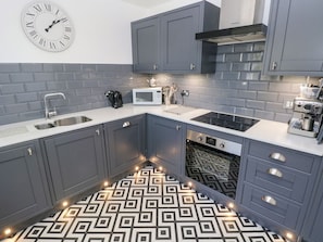 Ett modernt kök med grå skåp, en vit bänkskiva, ett mönstrat golv och en väggklocka.
