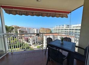 A balcony with a table and chairs, a view of buildings, and a clear sky.