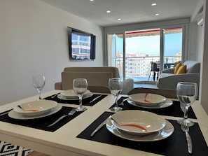 A dining area with a table set for four, a sofa, and a TV mounted on the wall.