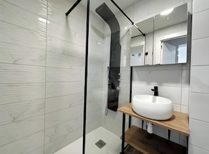 A modern bathroom with a glass-enclosed shower, a white sink on a wooden shelf, and a mirrored cabinet.