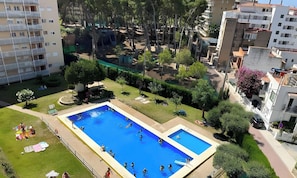 A residential area with two swimming pools, surrounded by greenery and adjacent to apartment buildings.