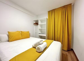 Una habitación de hotel con una cama, un armario blanco, una cortina amarilla y una toalla blanca sobre la cama.